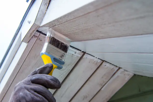 A handyman painting the eaves of a home.