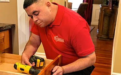 A Mr. Handyman technician fixing a drawer using a drill.