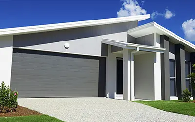 A house with a large garage painted in shades of gray beneath a bright blue sky.
